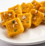 Moong Dal Barfi served on brass plate with saffron strands and cardamom pods